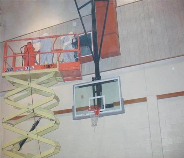 Three people on a metal scaffold wearing protective uniforms when performing fire cleanup in a gym